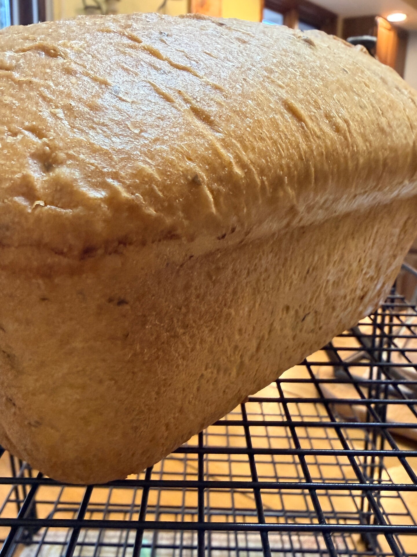 A close-up of a freshly baked loaf of bread cooling on a black wire rack in a warmly lit kitchen.