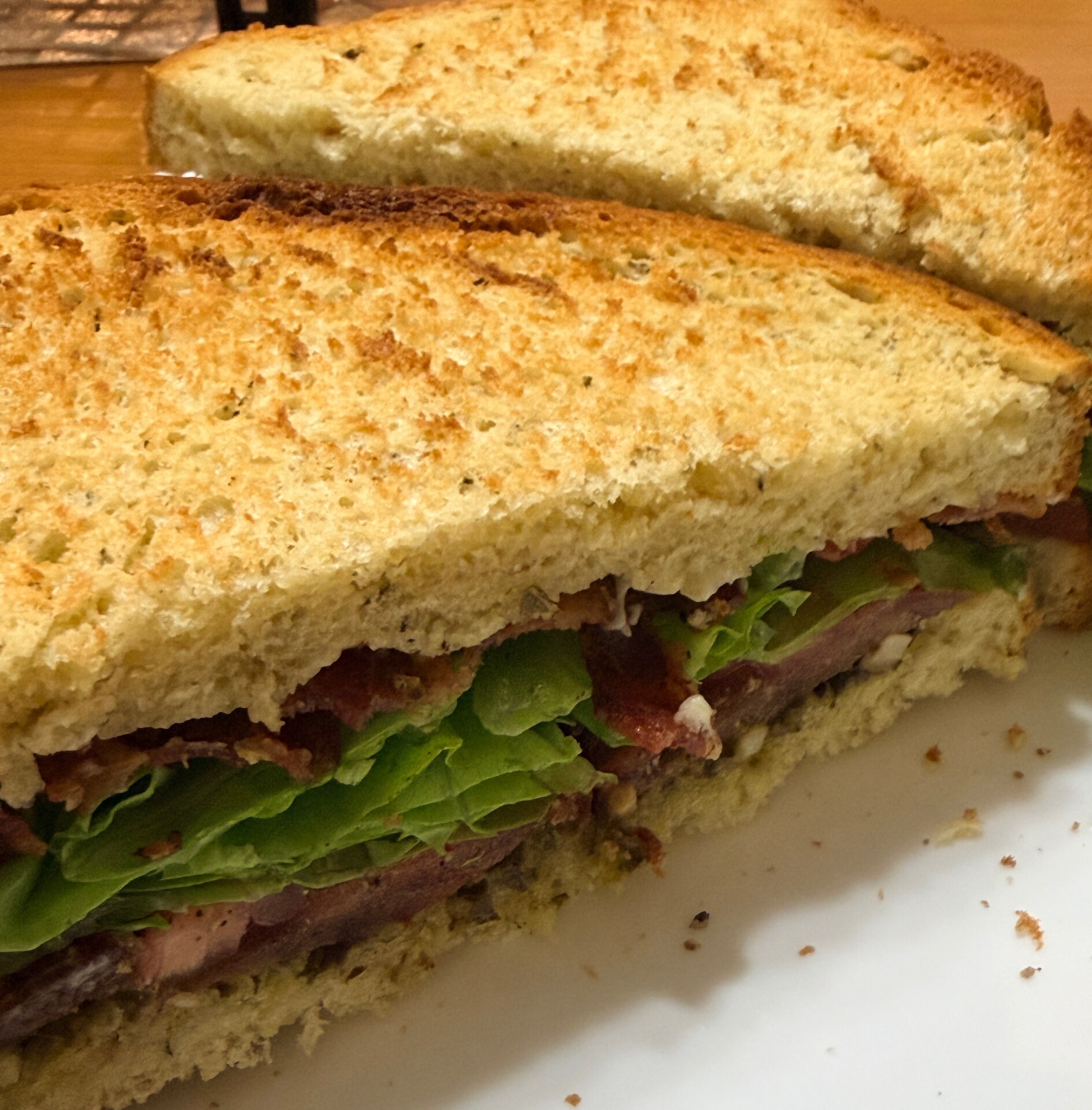 A close-up of a toasted sandwich cut in half, filled with lettuce, bacon, and possibly slices of tomato or meat, on a white plate.