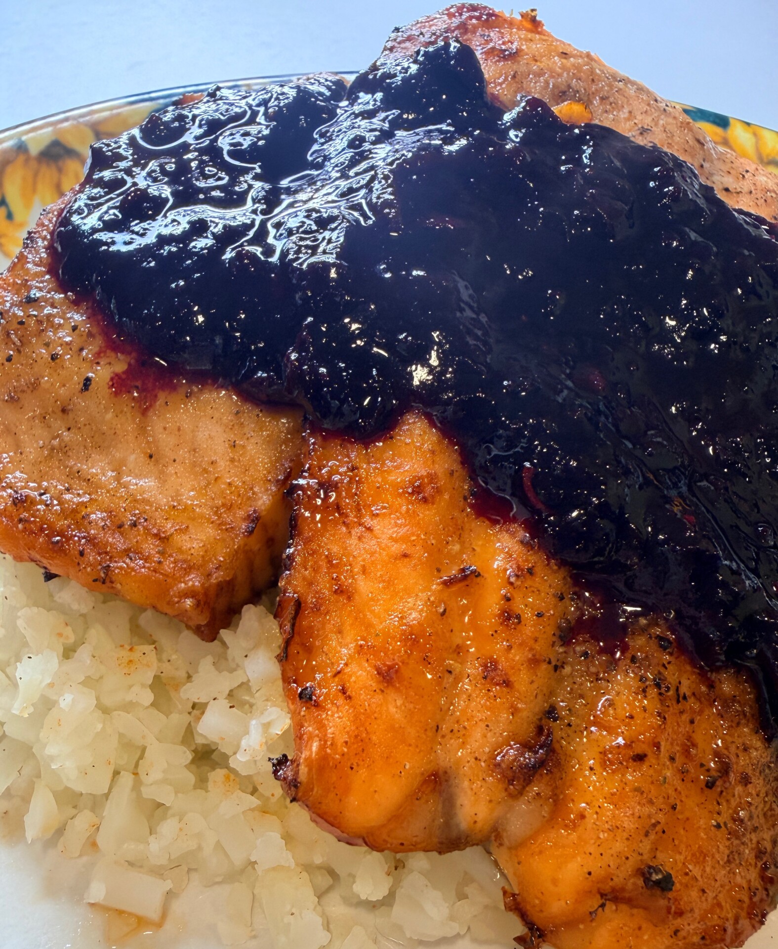 Grilled salmon fillets served on a bed of rice, topped with a thick, glossy blueberry sauce.