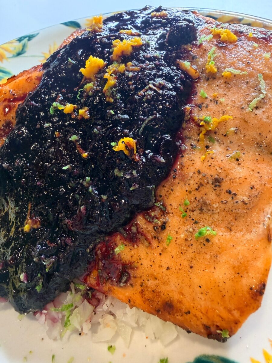 Grilled salmon fillet topped with a thick, dark berry sauce and orange zest, served on a bed of rice.