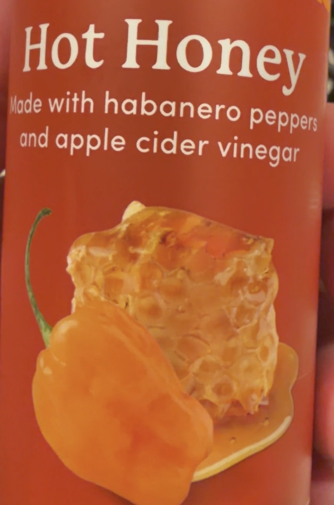 A label reads Hot Honey made with habanero peppers and apple cider vinegar with images of a habanero pepper and a honeycomb on a red background.