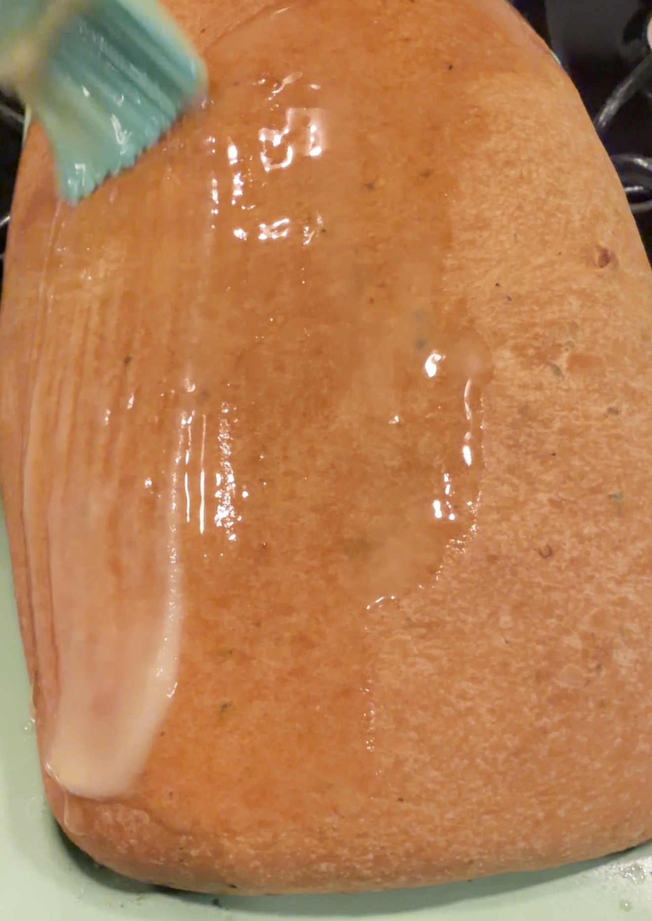 A close-up of a baked loaf of bread being brushed with melted butter, giving the crust a shiny, golden appearance.