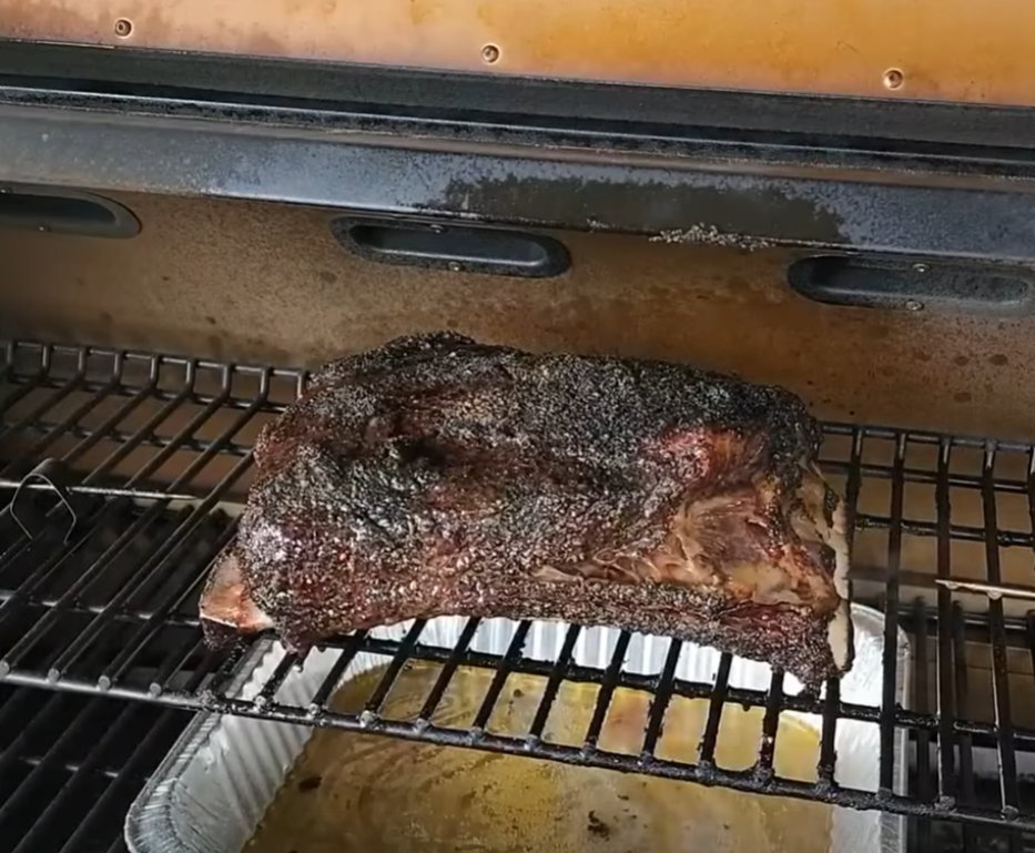A large, seasoned brisket is being smoked on a grill rack, with a disposable foil pan underneath to catch drippings.