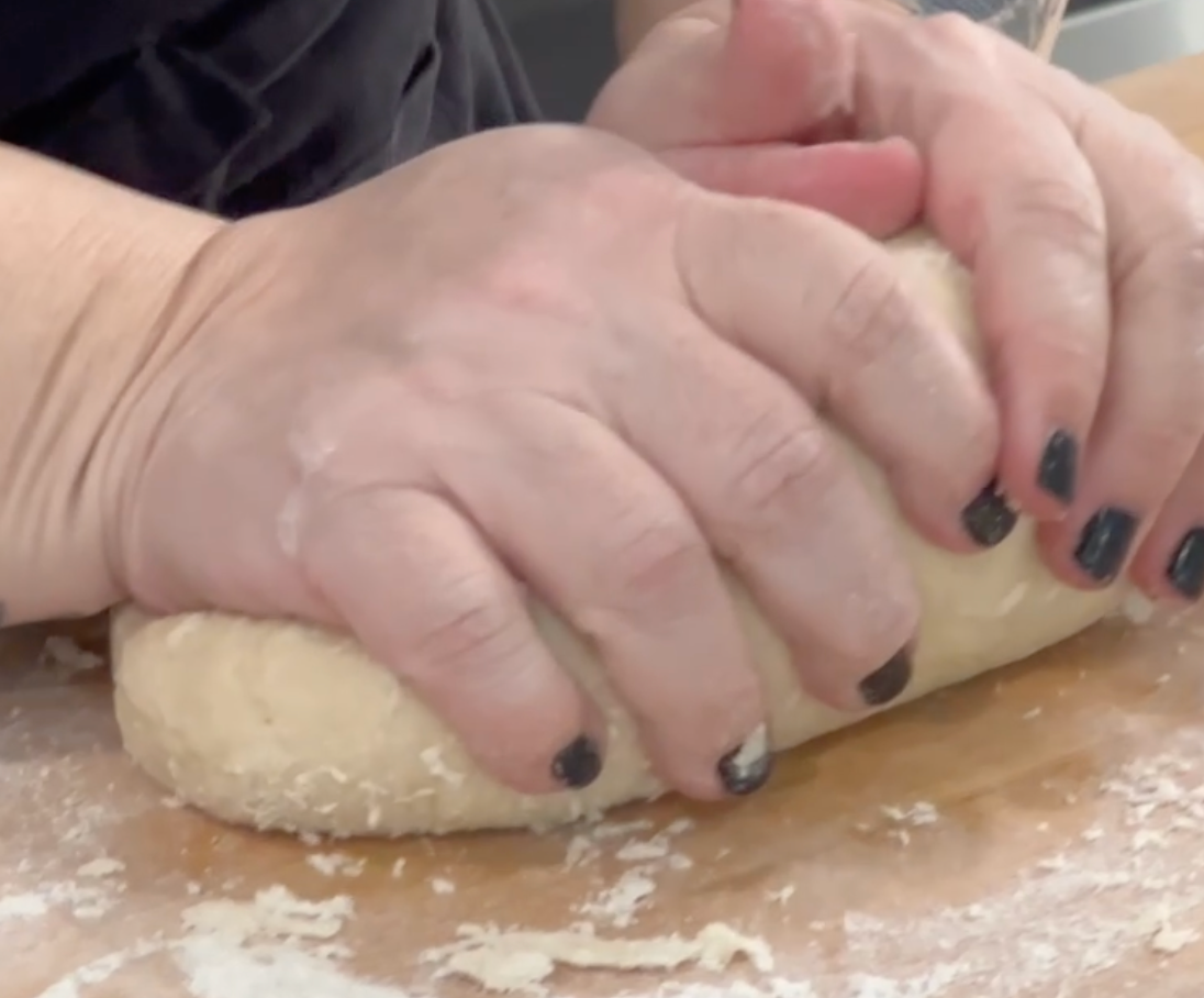 Hands with black nail polish kneading dough on a floured surface.