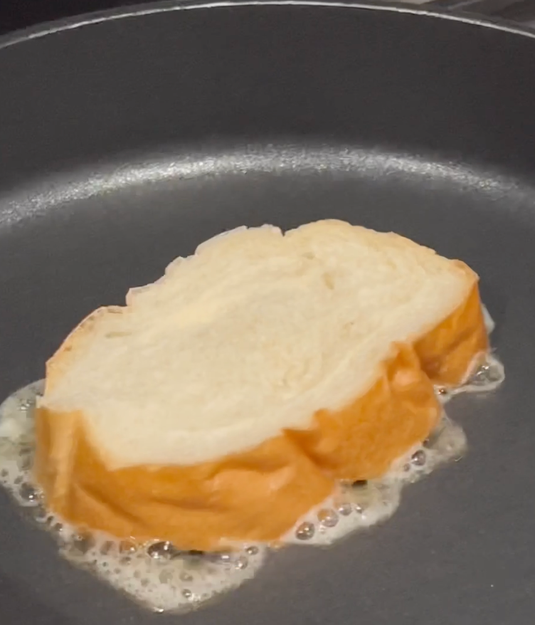 A slice of bread is frying in a pan with melted butter bubbling around its edges.