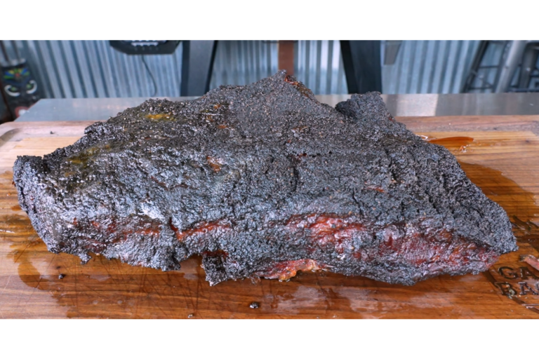 A large smoked brisket with a dark, crispy bark rests on a wooden cutting board, showing juicy meat and rendered fat.