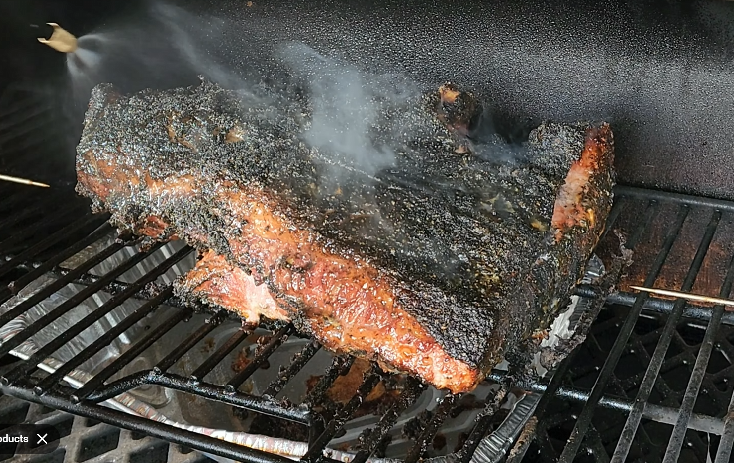 A large piece of brisket with a dark, crispy bark is smoking on a grill rack, with visible smoke wafting around the meat inside a smoker.
