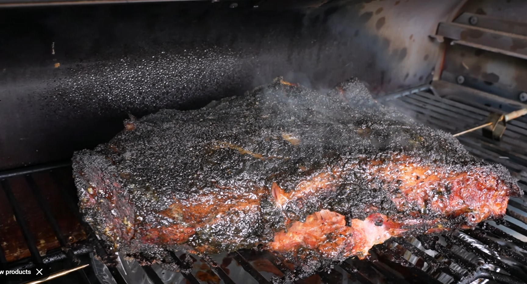 A smoked brisket with a dark, crispy bark cooks on a metal grill inside a smoker, with smoke rising around the meat.