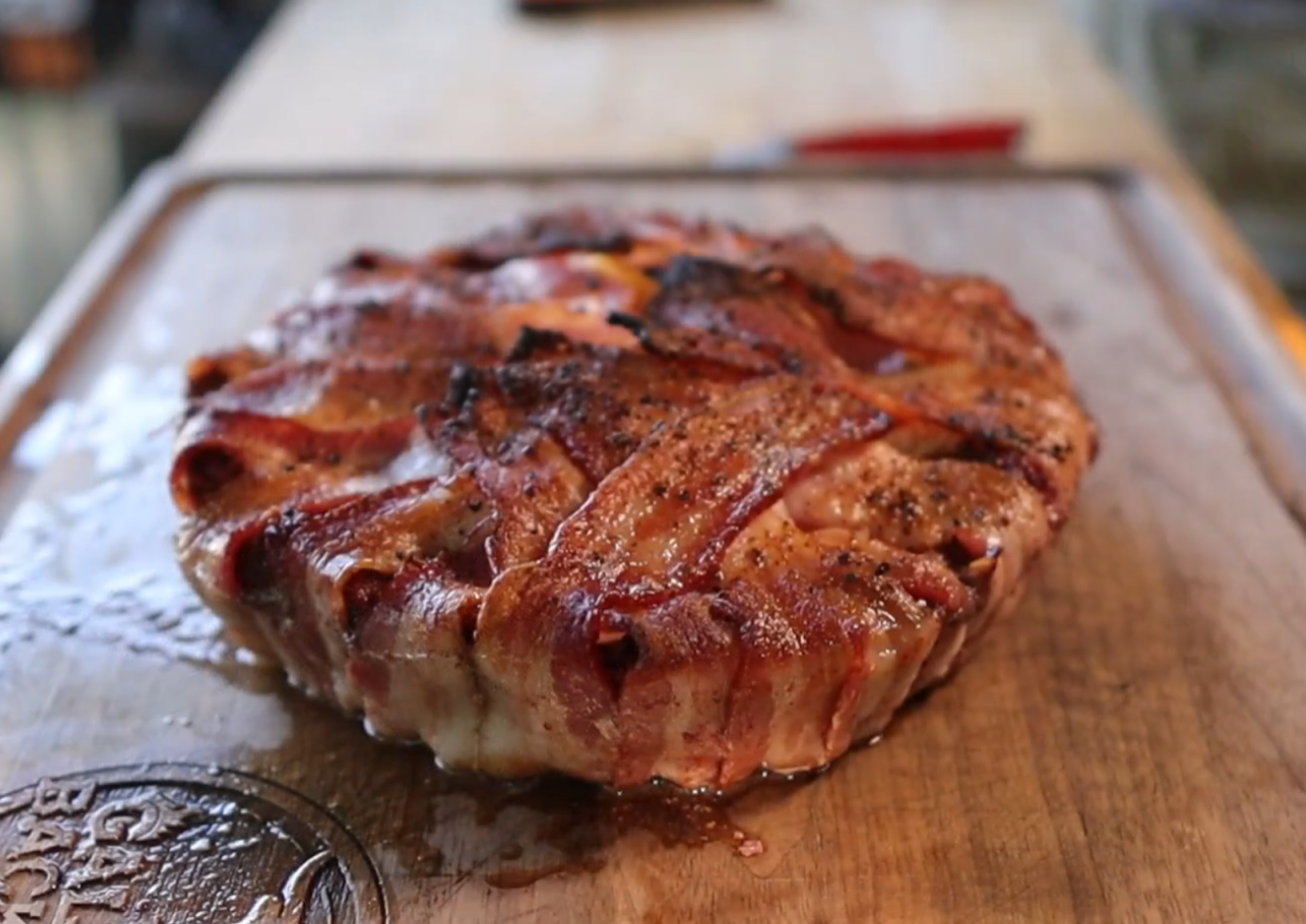 A pie or tart covered with crispy, cooked bacon strips sits on a wooden cutting board, glistening with juices.