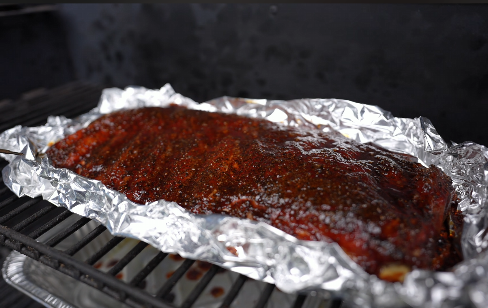 A rack of barbecued ribs coated in sauce sits on aluminum foil atop a grill, ready to be cooked or served.
