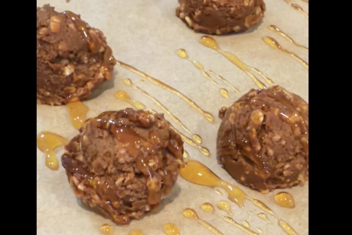 Scoops of chunky chocolate cookie dough with nuts are placed on parchment paper, drizzled with golden caramel sauce.