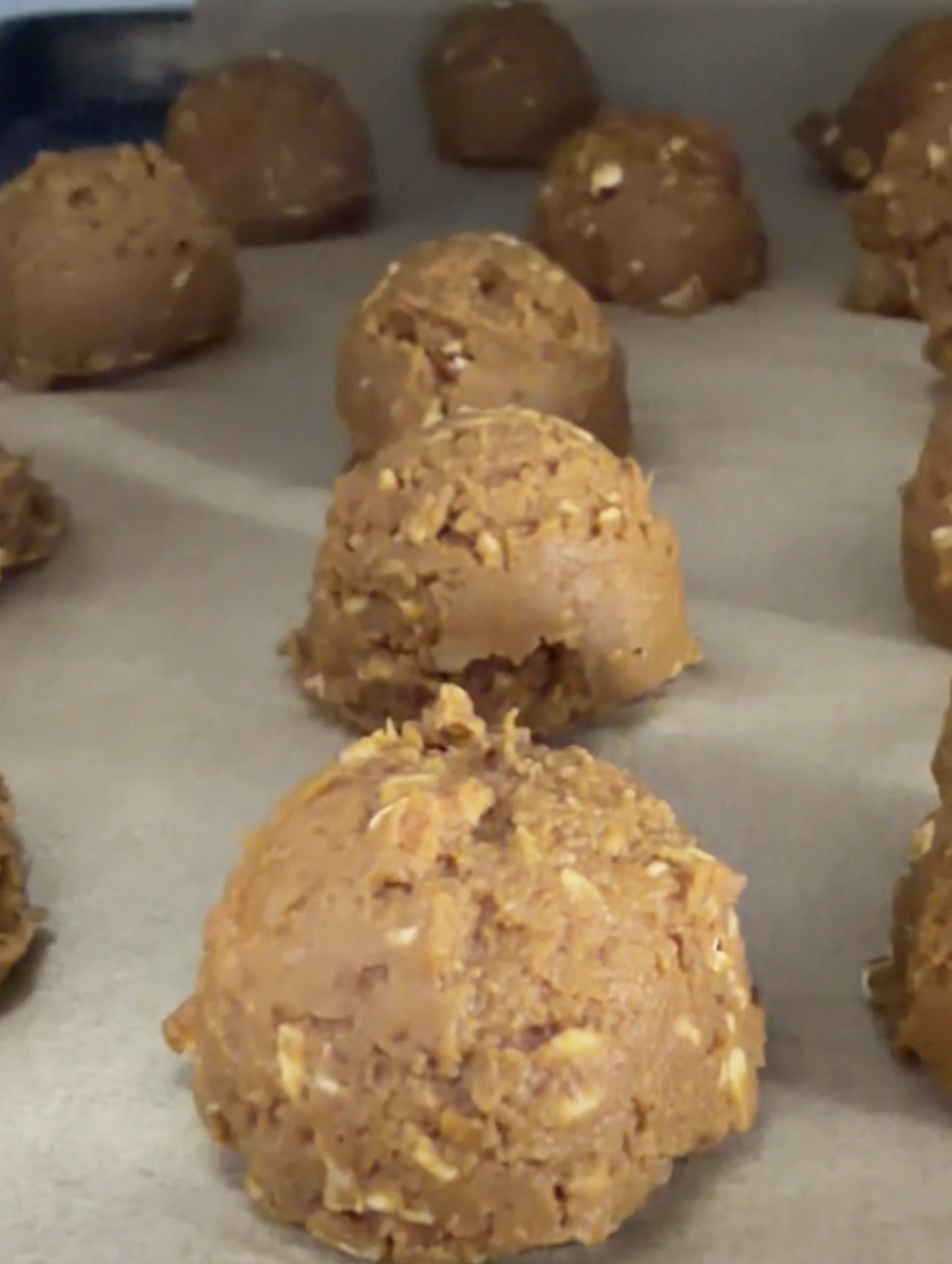 Scoops of oatmeal peanut butter cookie dough arranged on a baking sheet lined with parchment paper, ready to be baked.
