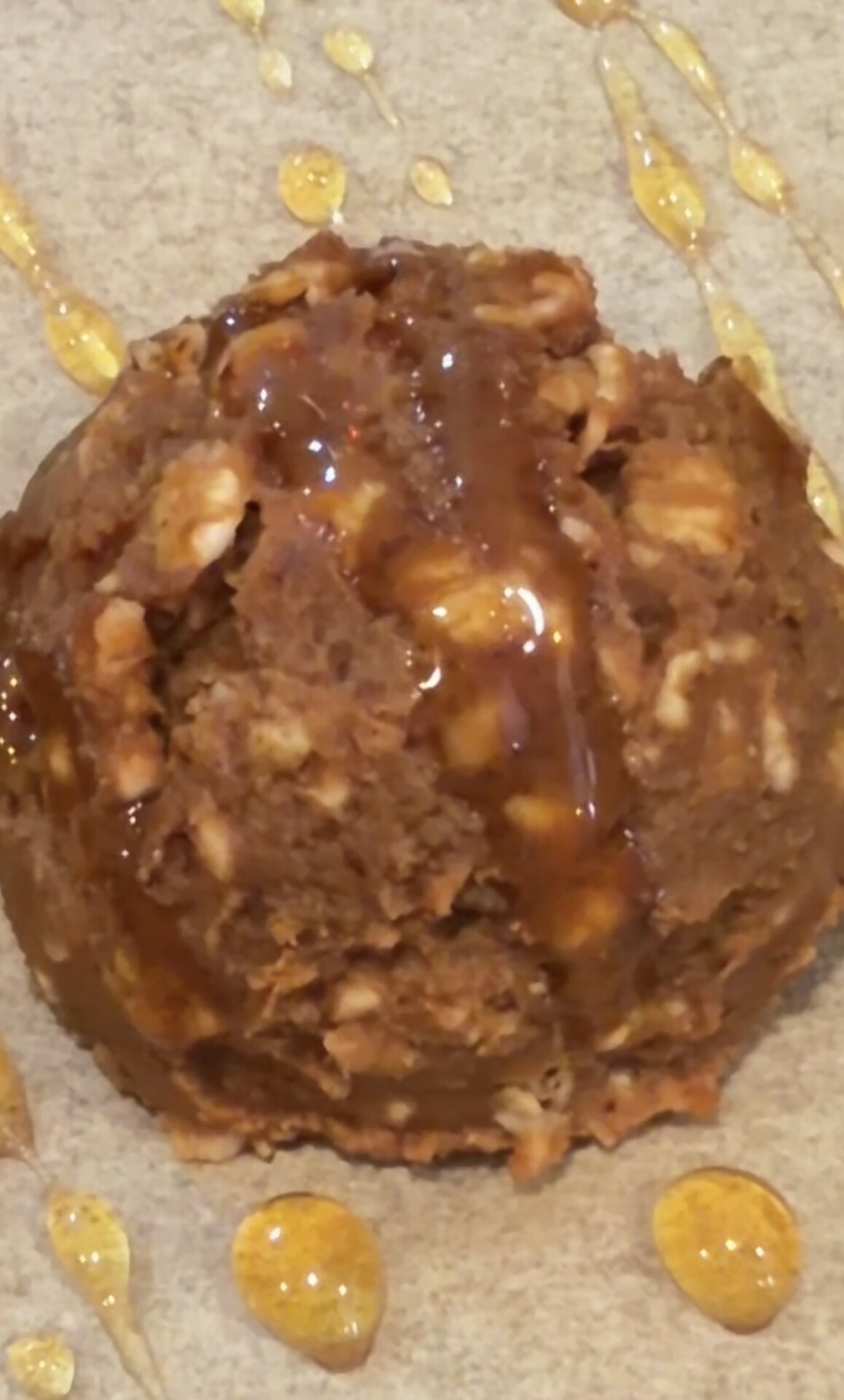 A scoop of chunky brown cookie dough with visible oats, drizzled with golden honey on a parchment surface.