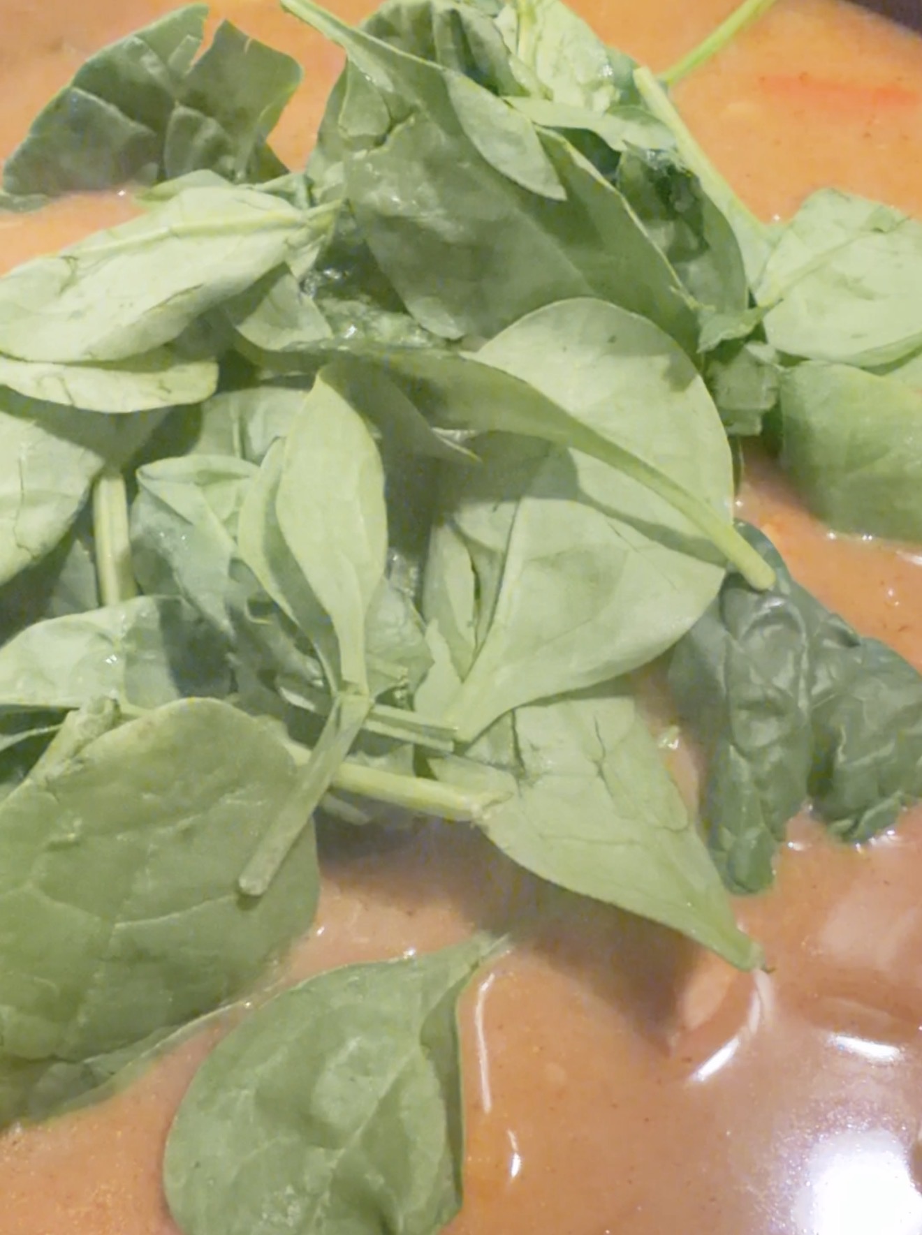 Fresh spinach leaves floating on top of a light brown creamy soup or sauce.