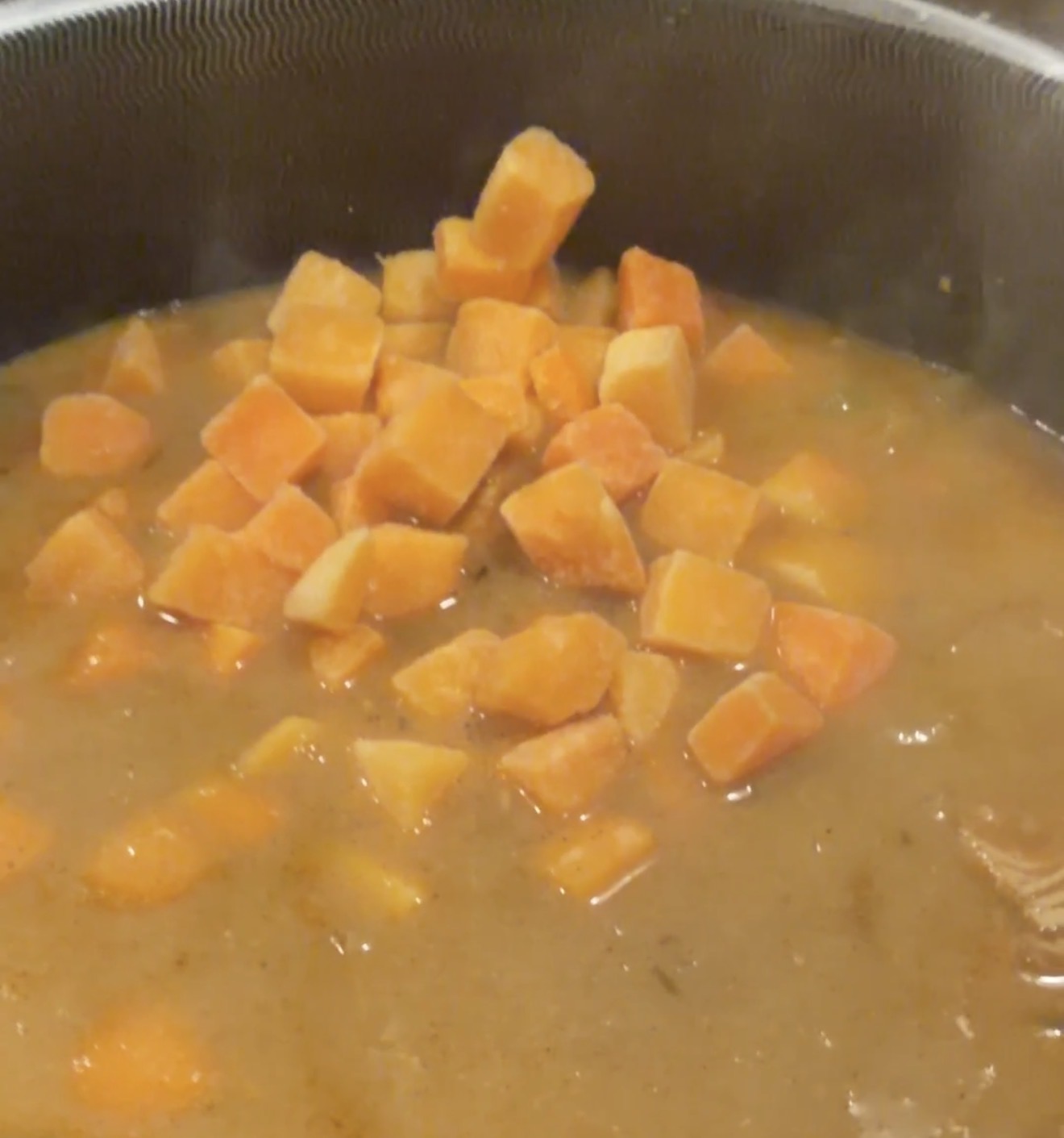Diced sweet potatoes simmering in a pot of broth, partially submerged and cooking.
