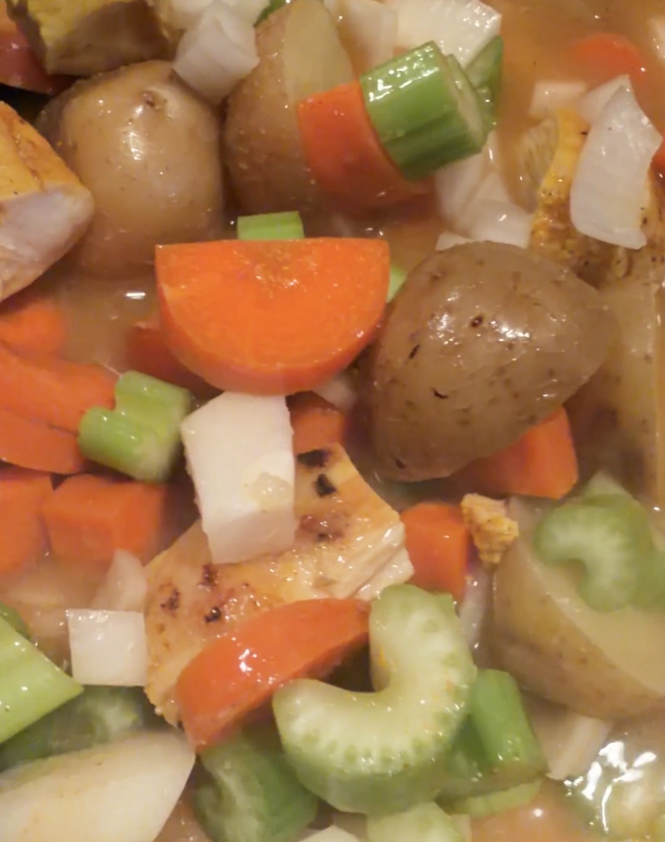 A close-up of a hearty stew with chunks of potato, carrots, celery, onions, and pieces of cooked chicken in a savory broth.
