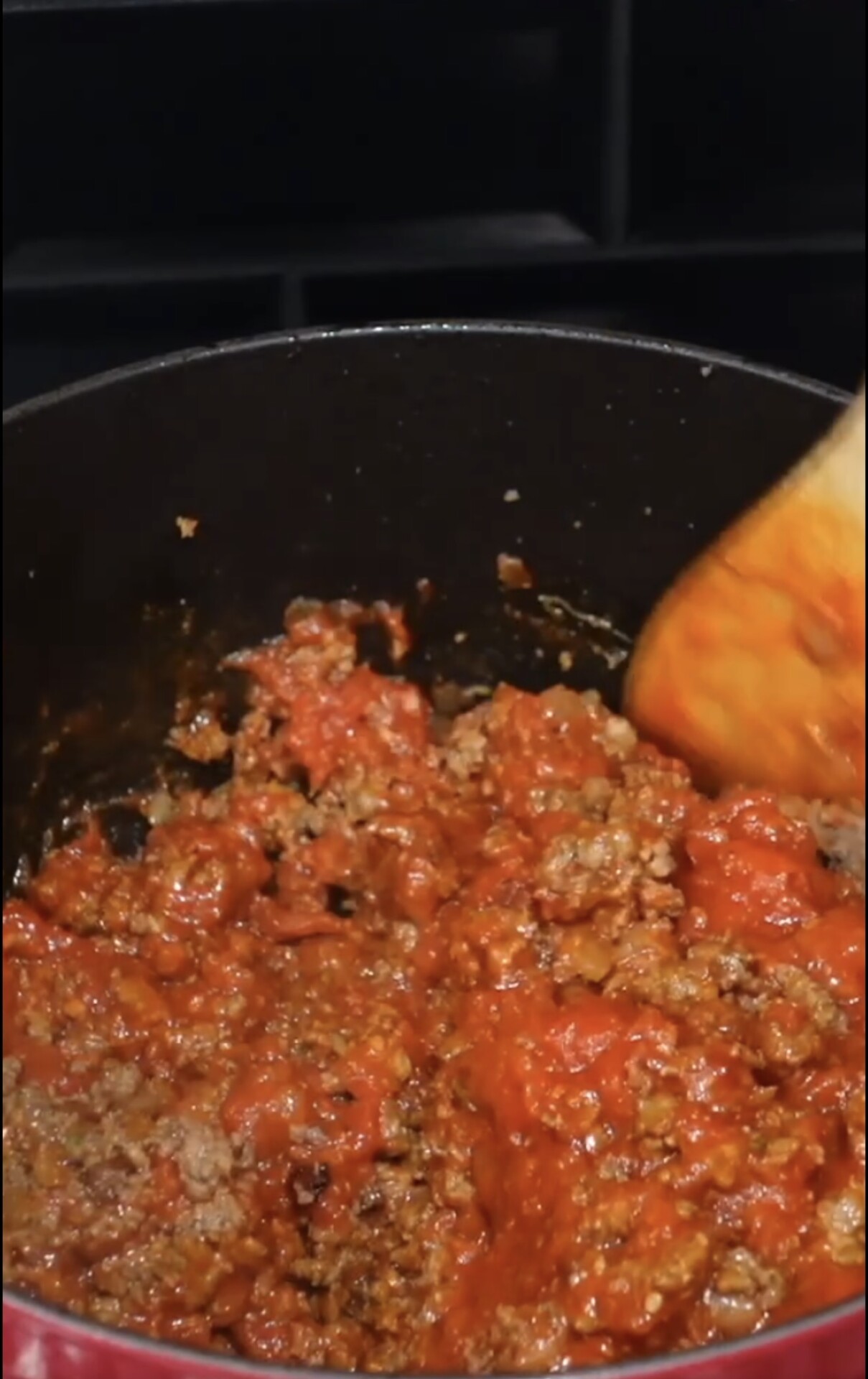 Ground beef and tomato sauce being stirred in a pot with a wooden spoon, during the process of cooking a meat sauce.
