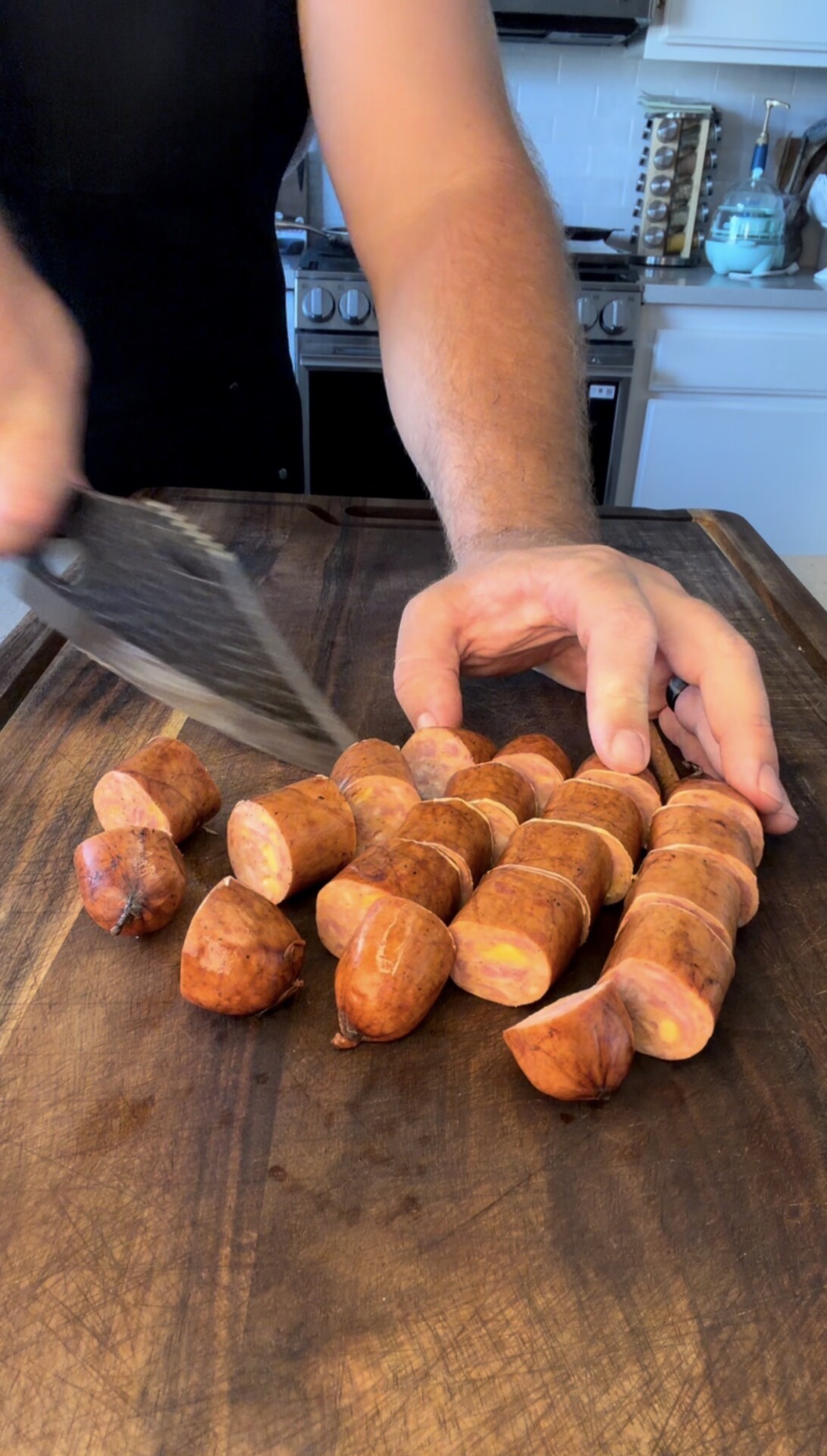 A person slices sweet potatoes with a knife on a wooden cutting board in a kitchen, creating evenly sized pieces.