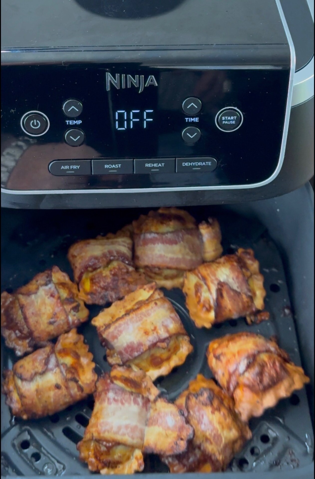 Bacon-wrapped snacks are cooked in an air fryer basket, with the Ninja air fryer display reading OFF..