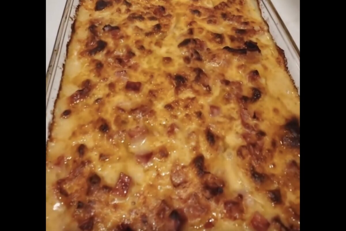 A close-up of a baked casserole topped with melted, browned cheese and diced pieces of ham in a rectangular glass dish.