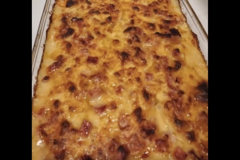 A close-up of a baked casserole topped with melted, browned cheese and diced pieces of ham in a rectangular glass dish.