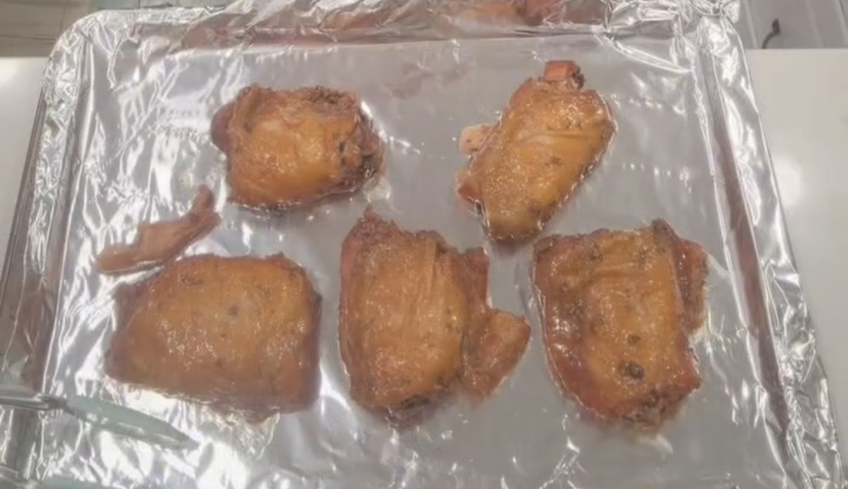 Five pieces of cooked, browned chicken sit on a foil-lined baking sheet.