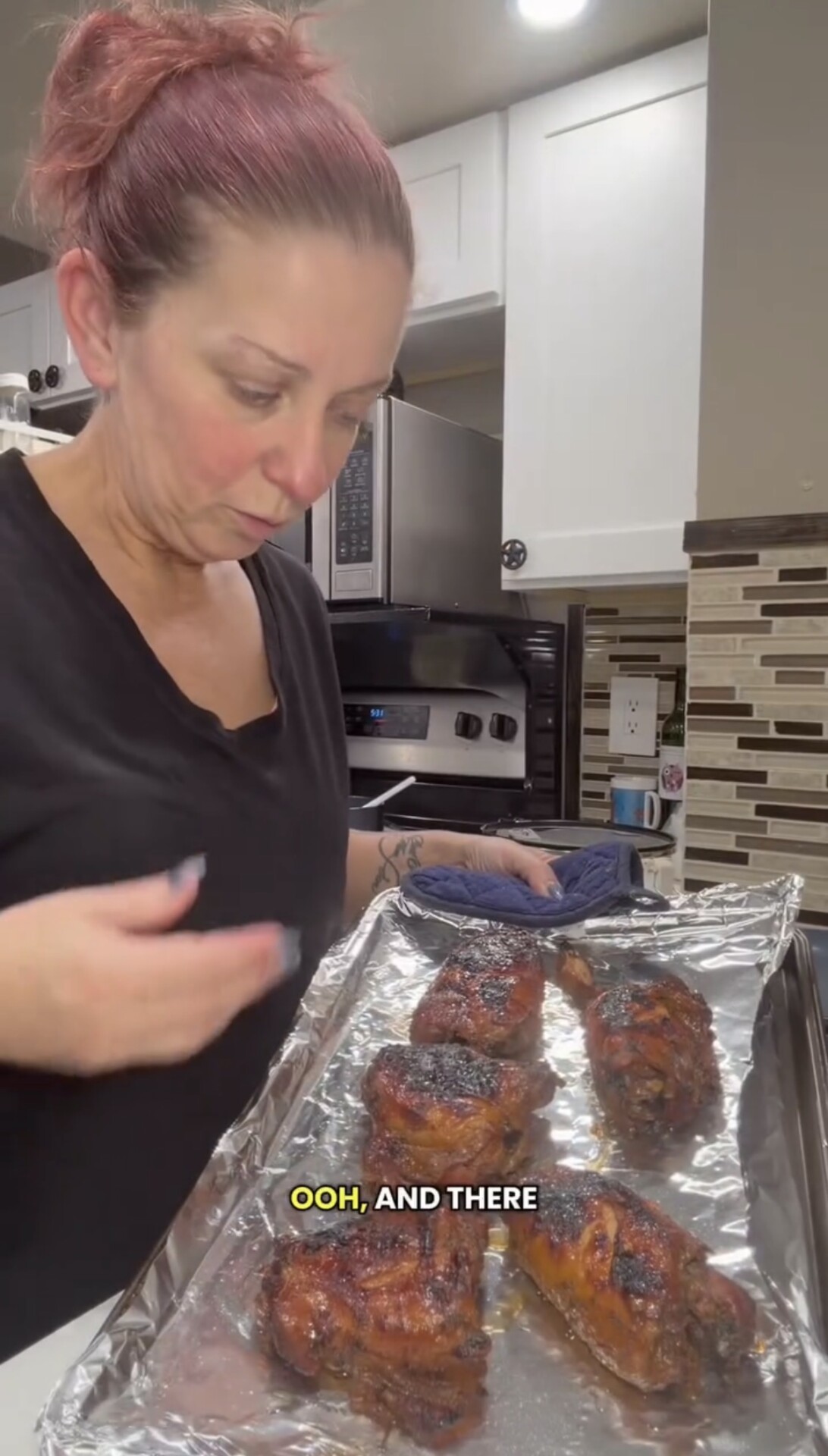 A woman with red hair holds a tray of cooked, browned meat pieces on foil in a kitchen. Captions on the image read, OOH, AND THERE..