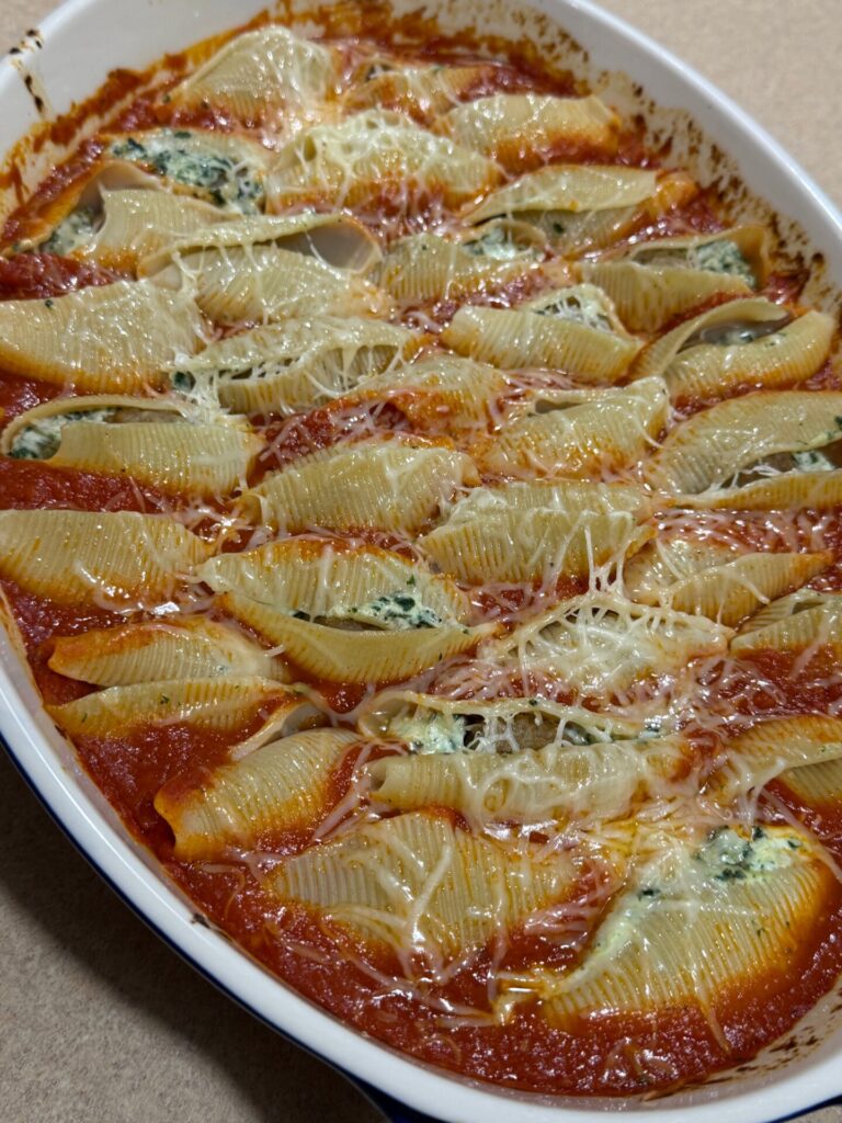 A baking dish filled with jumbo pasta shells stuffed with ricotta and spinach, topped with tomato sauce and melted cheese.