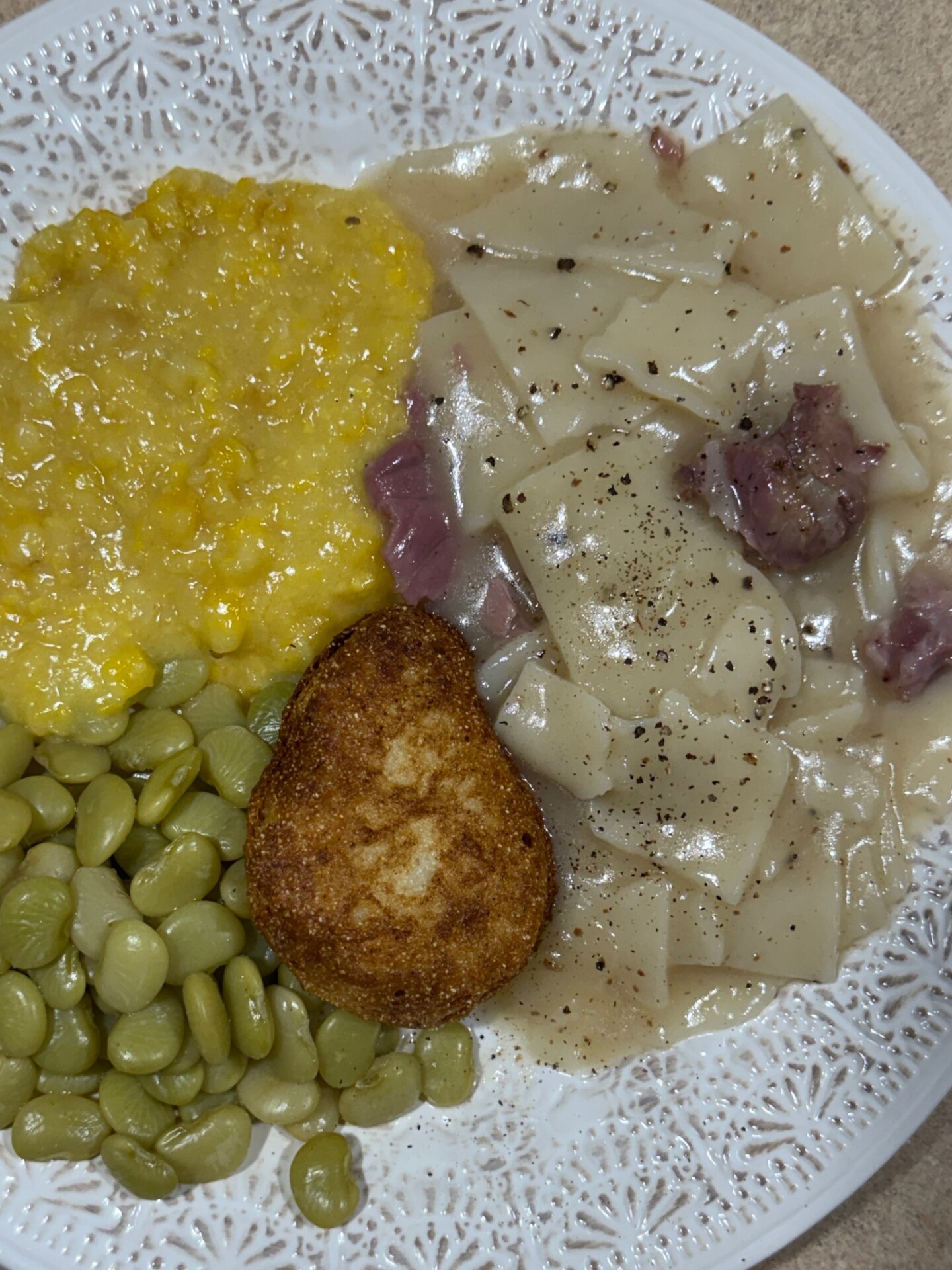 A white plate with lima beans, creamed corn, a breaded fried item, and homemade noodle soup with beef chunks and black pepper.