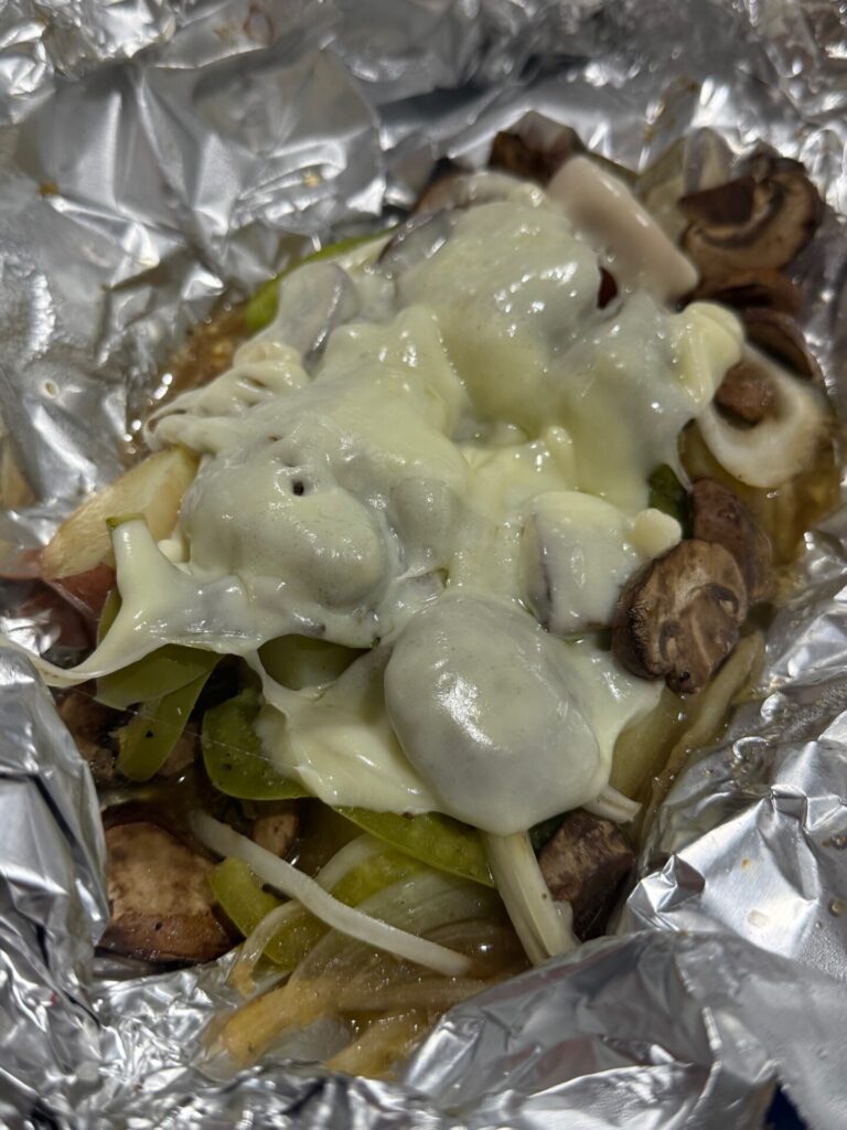 Sliced mushrooms, onions, and green peppers, topped with melted cheese, served on foil.