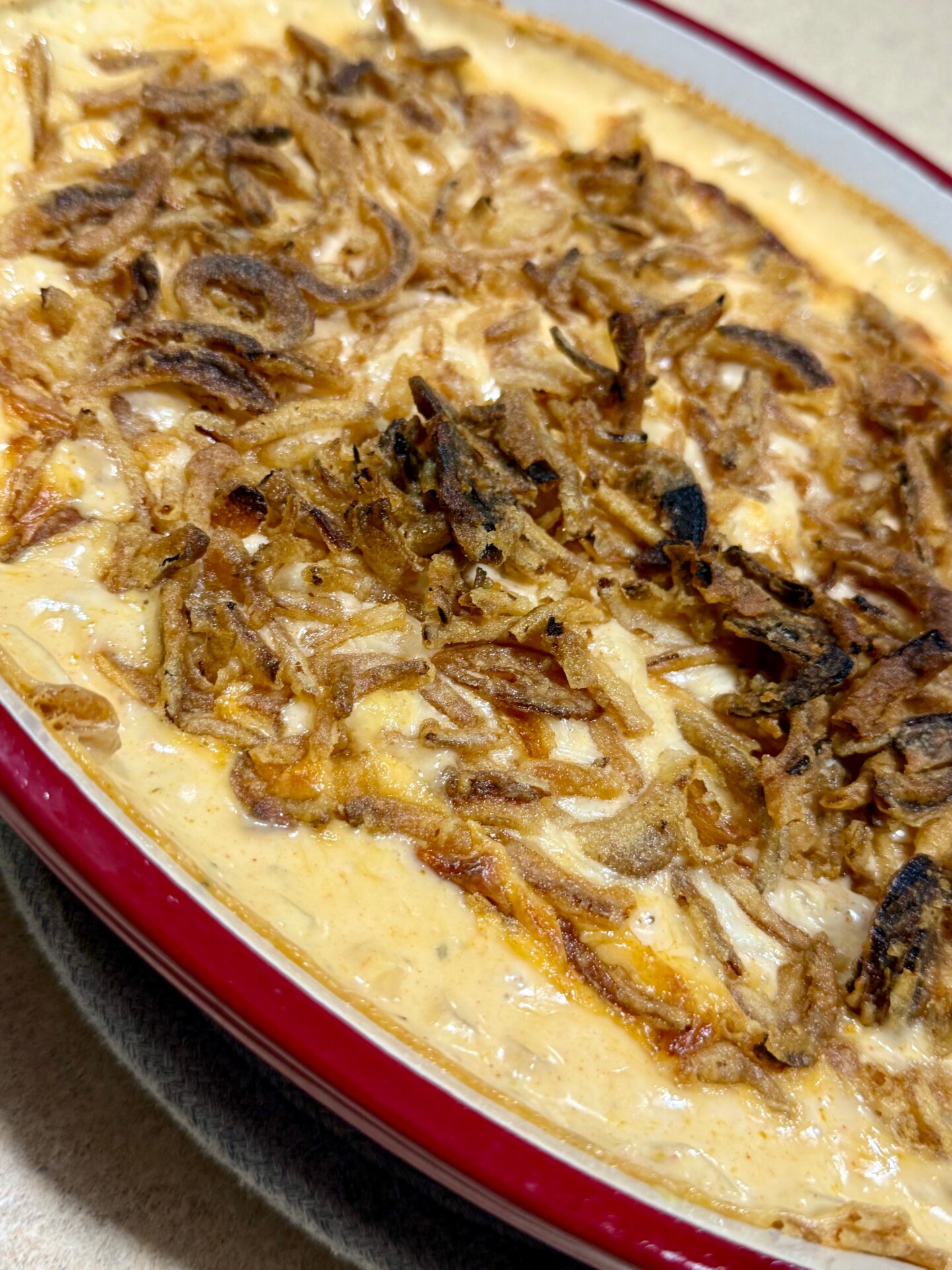 A close-up of a creamy casserole topped with crispy fried onions in a red-edged baking dish.