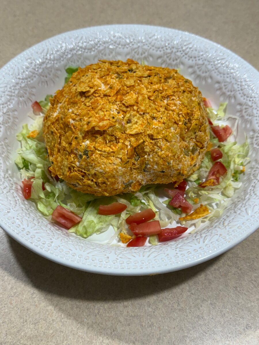 A round, orange-crusted ball sits on chopped lettuce and diced tomatoes in a white textured bowl, placed on a tan countertop.