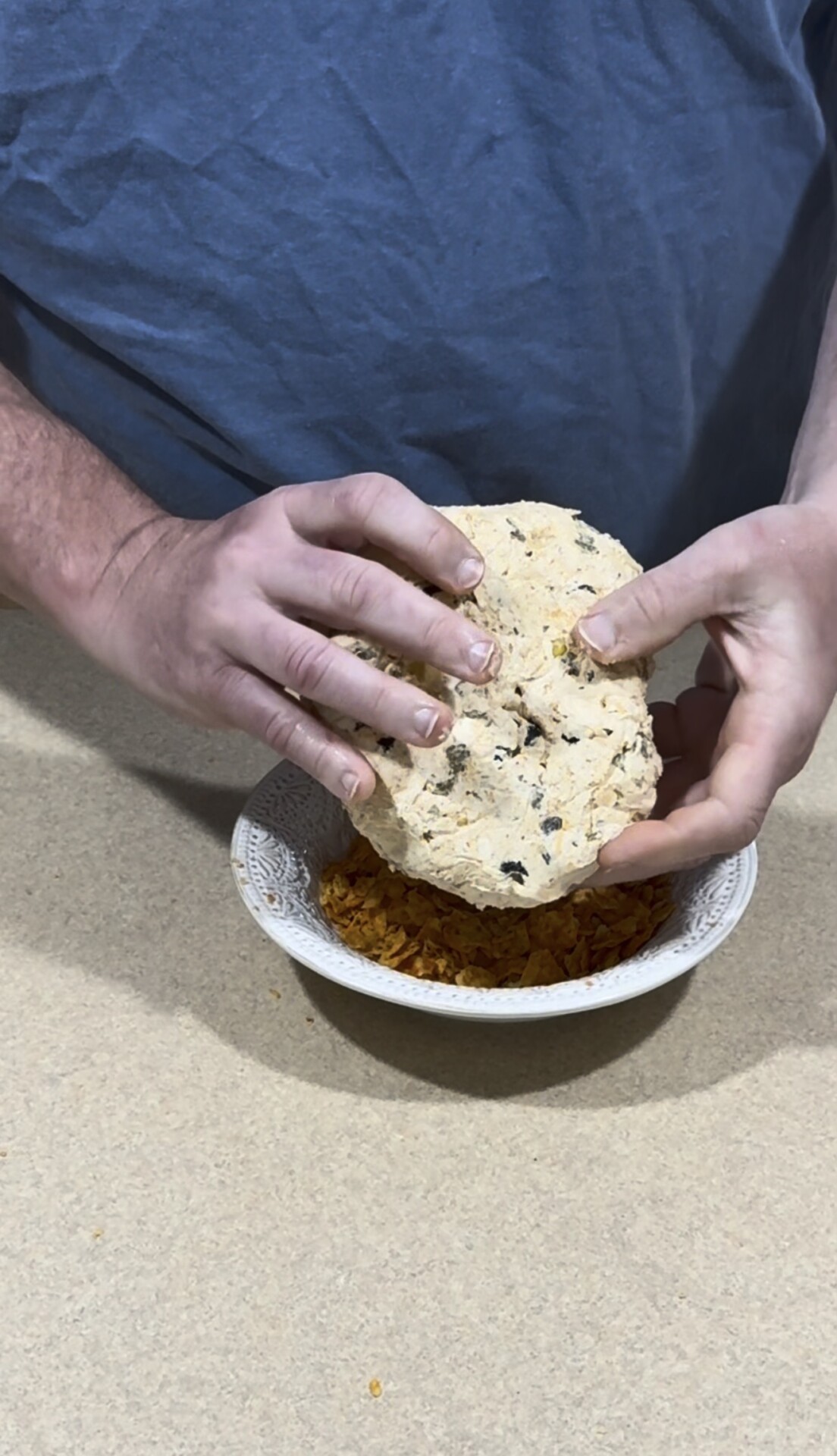 A person in a blue shirt holds a round, flatbread-like food over a white bowl filled with orange rice, preparing to break the bread in half.