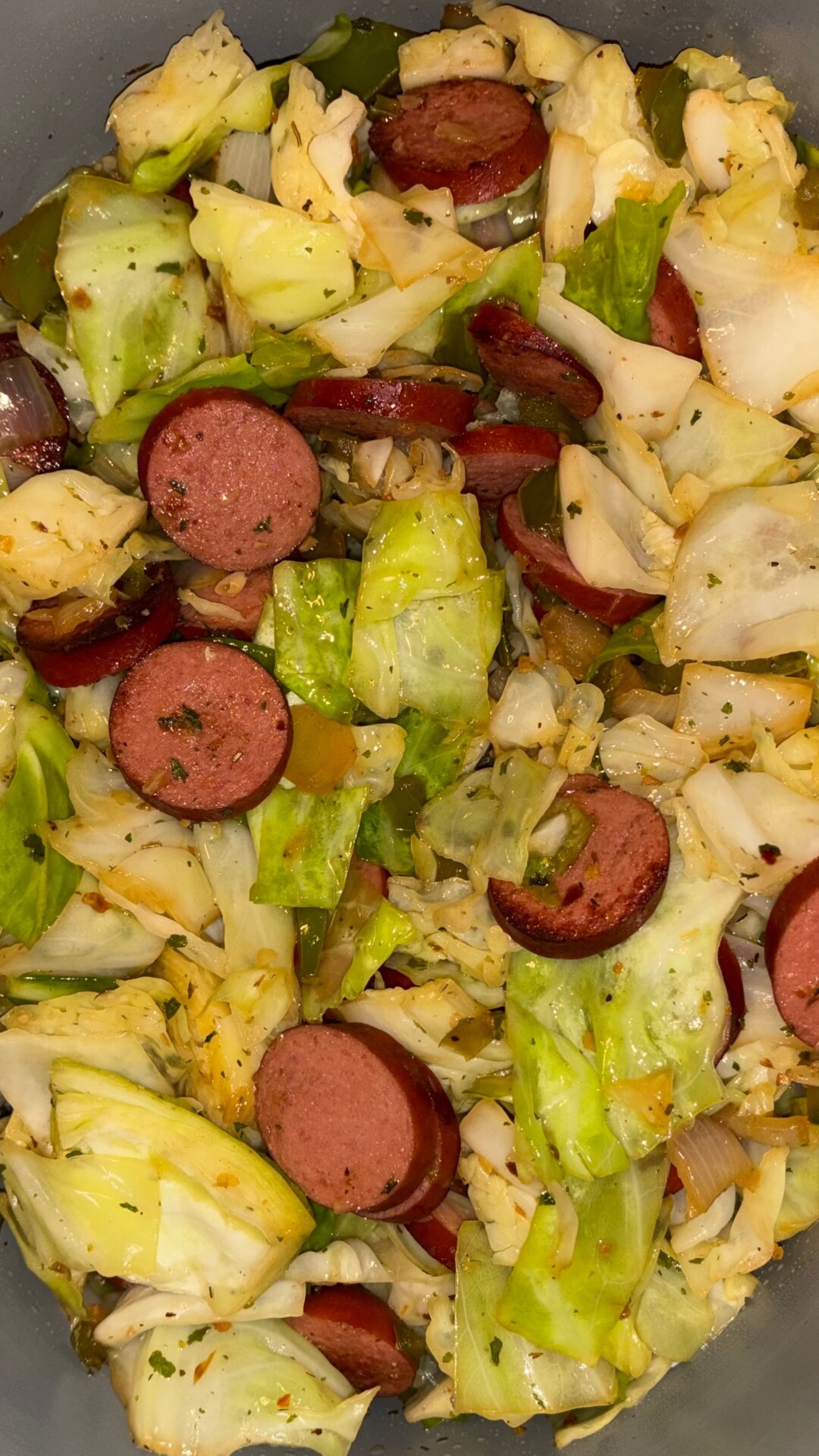 Chopped cabbage, sliced sausage, green bell peppers, and onions cooked together, seasoned with herbs, and served in a bowl.