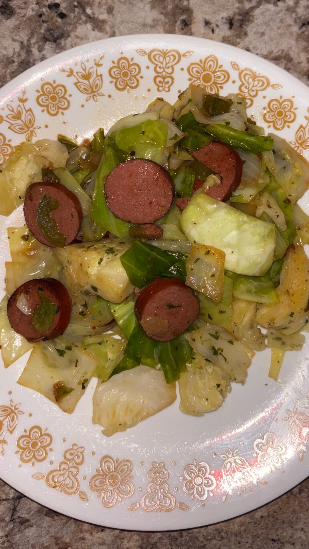 A plate of cooked cabbage mixed with sliced sausage and green bell peppers, served on a white plate with a yellow floral pattern.