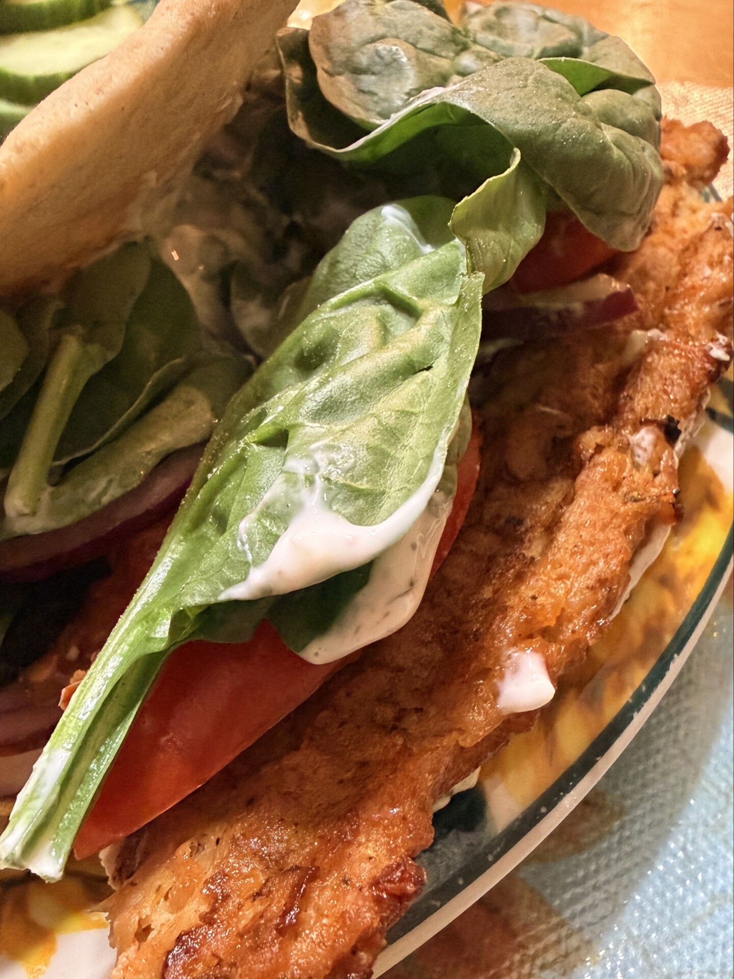 Breaded chicken cutlet sandwich with fresh spinach, tomato slices, red onion, and creamy sauce.