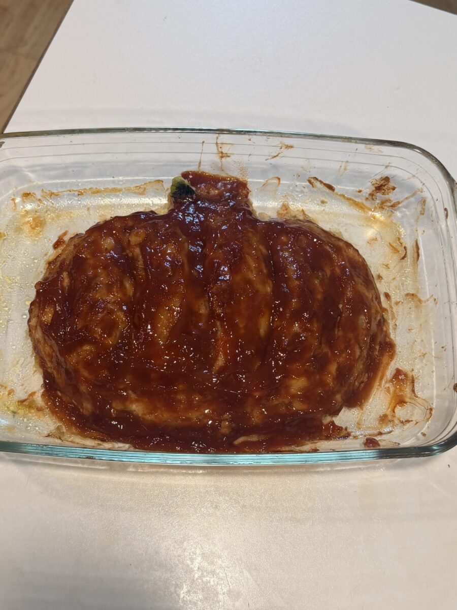 Meatloaf topped with red glaze in a clear glass baking dish.