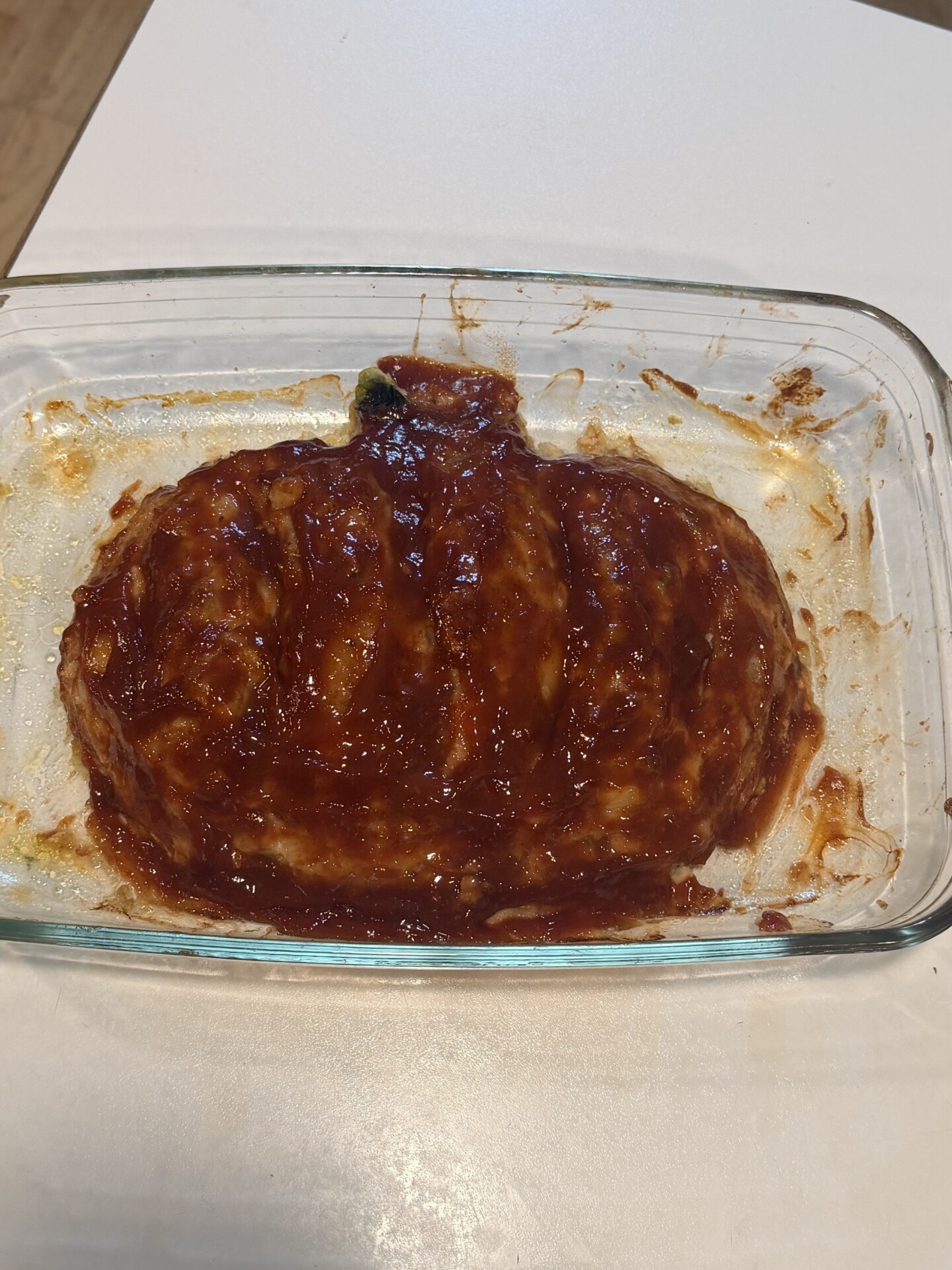 Meatloaf topped with red glaze in a clear glass baking dish.