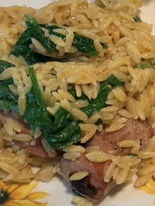 Orzo pasta mixed with spinach and sliced sausage.