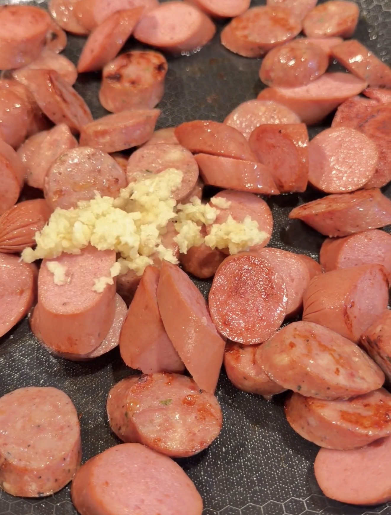 Sliced sausage links browning in a pan with a pile of minced garlic in the center.