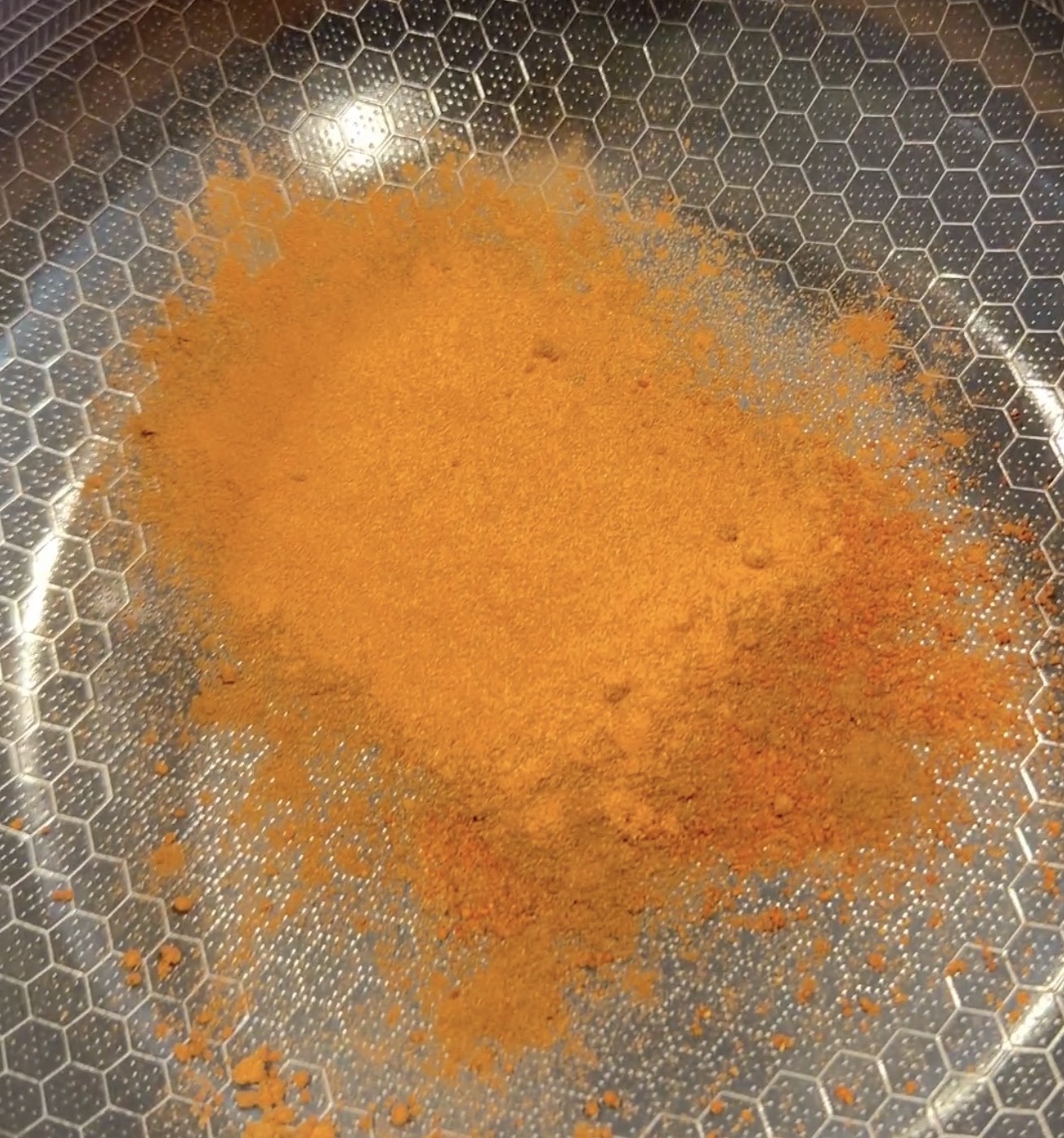 A pile of bright orange spice powder in a metal pan with a hexagonal texture.