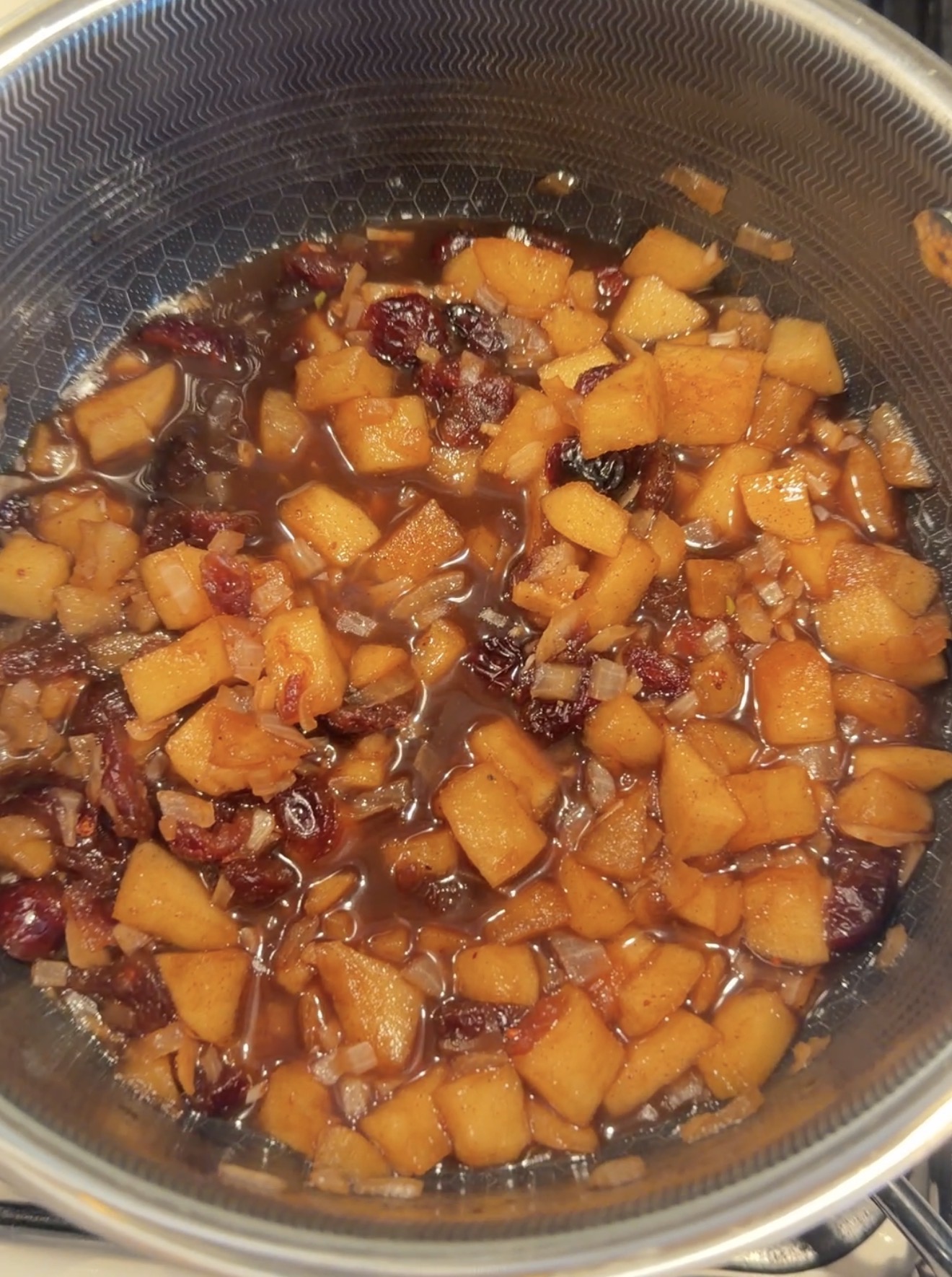 A pot filled with a cooked mixture of diced apples, onions, and dried cranberries in a dark sauce.