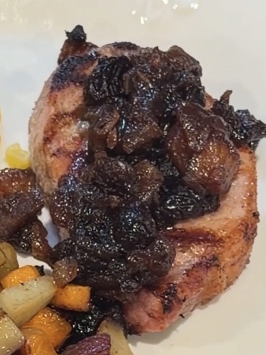 A grilled pork chop topped with a dark fruit glaze, served with a side of roasted root vegetables.