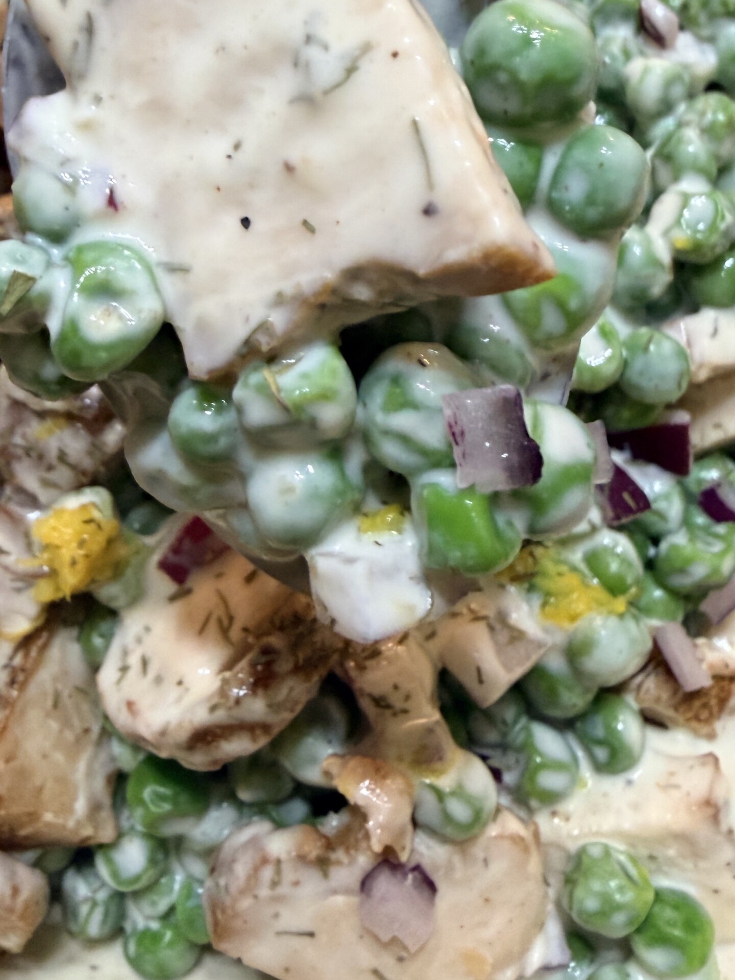 A spoonful of creamy salad containing green peas, diced chicken, mushrooms, and red onion.