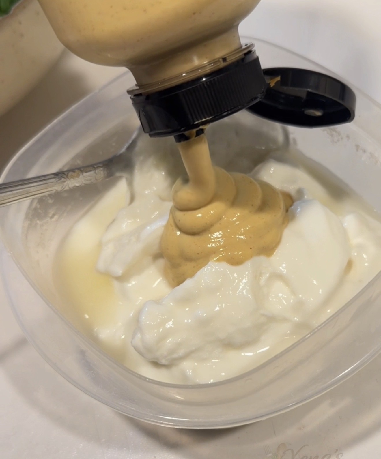 Mustard being squeezed from a bottle into a plastic container of plain yogurt.