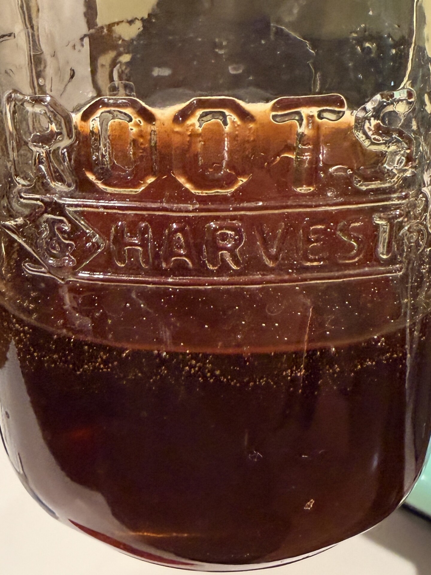 A glass jar labeled ROOTS & HARVEST containing dark liquid.