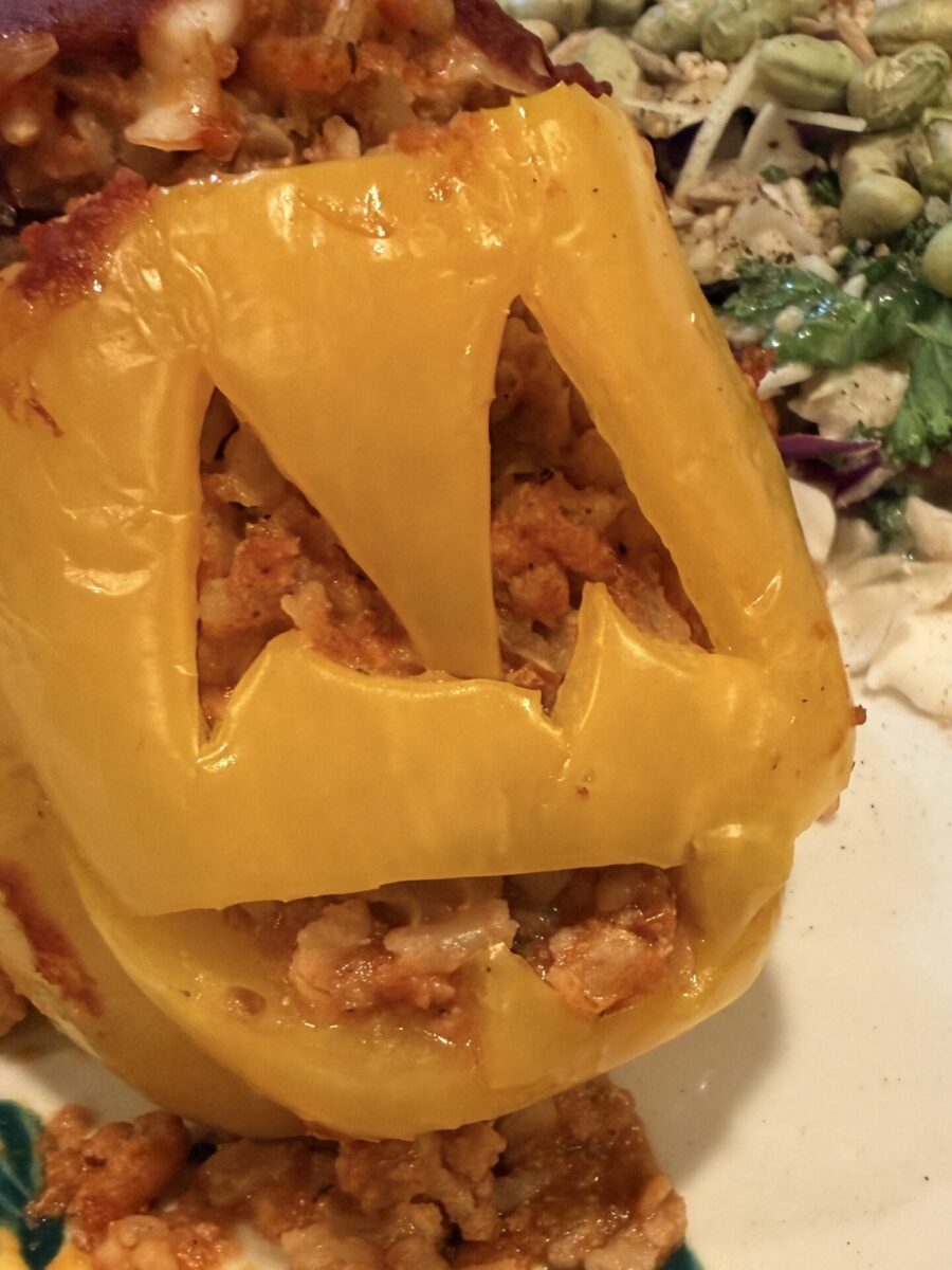 A yellow bell pepper carved like a jack-o-lantern and stuffed with a savory filling, served with a side of salad.