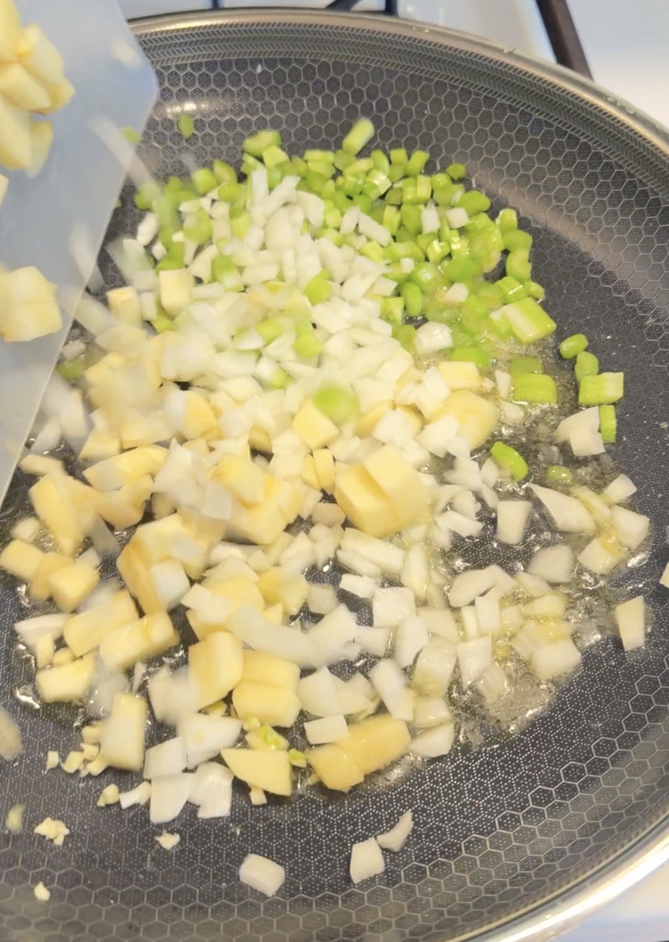 Diced onion, celery, and potatoes being poured from a cutting board into a hot skillet.