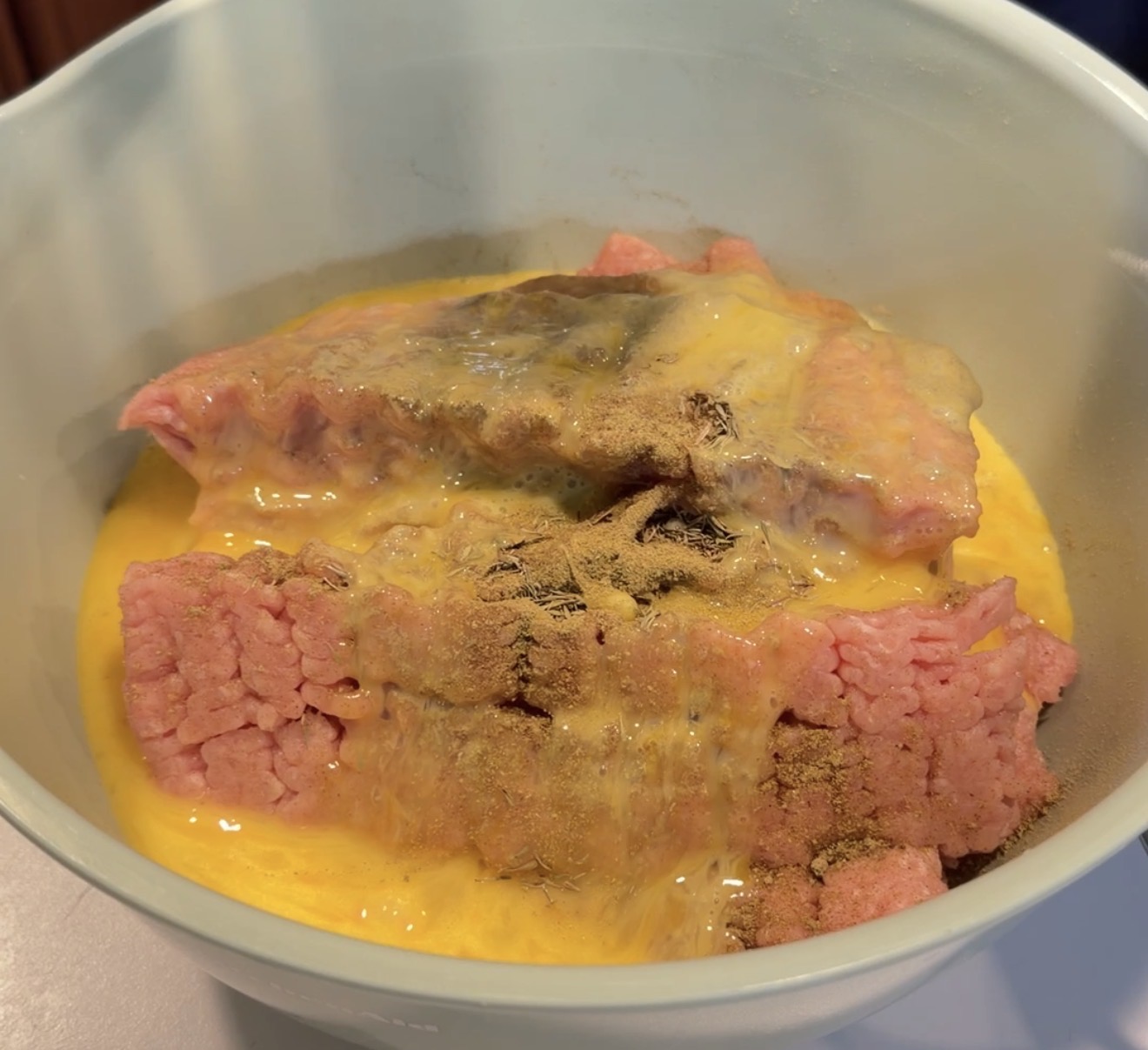 Raw ground meat in a mixing bowl with beaten eggs and a dusting of spices.