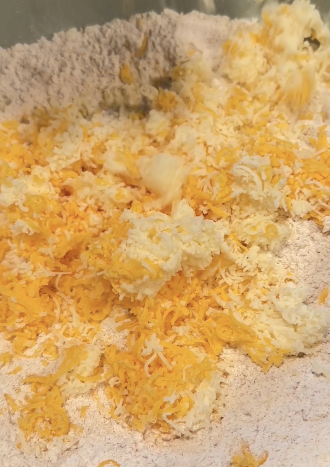 Shredded white and orange cheese mixed into a bowl of flour.